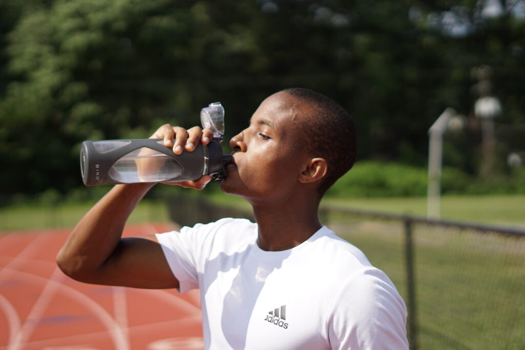 man in white crew neck t-shirt drinking water from black sports bottle on running track