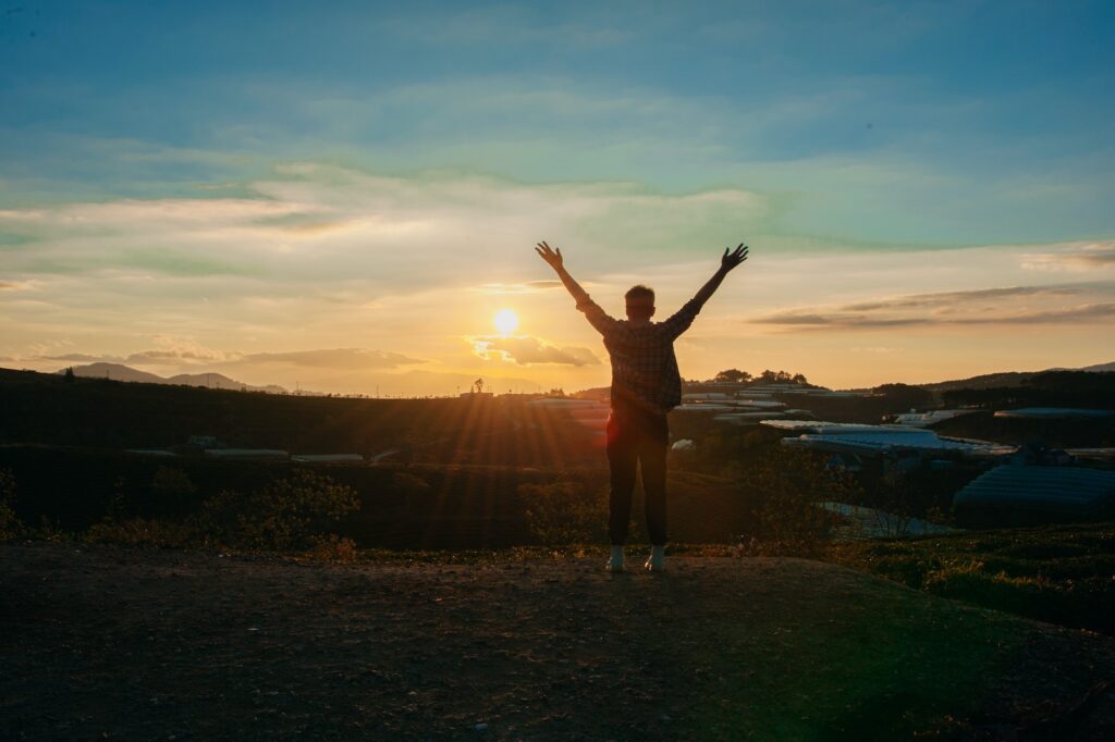 a silhouette of a man standing with hands raised at sunrise 