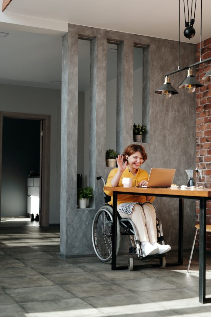 woman in wheelchair on a video chat on her laptop waving at the screen