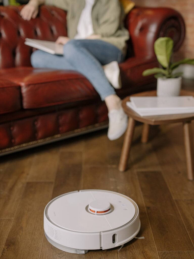 Person in Blue Denim Jeans Sitting on Red Sofa while their robot vacuum cleans the floor