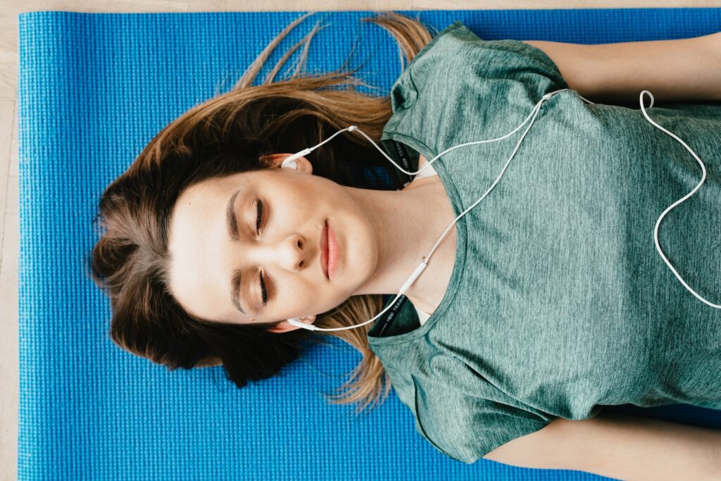 Tranquil woman resting on yoga mat listening to her earphones