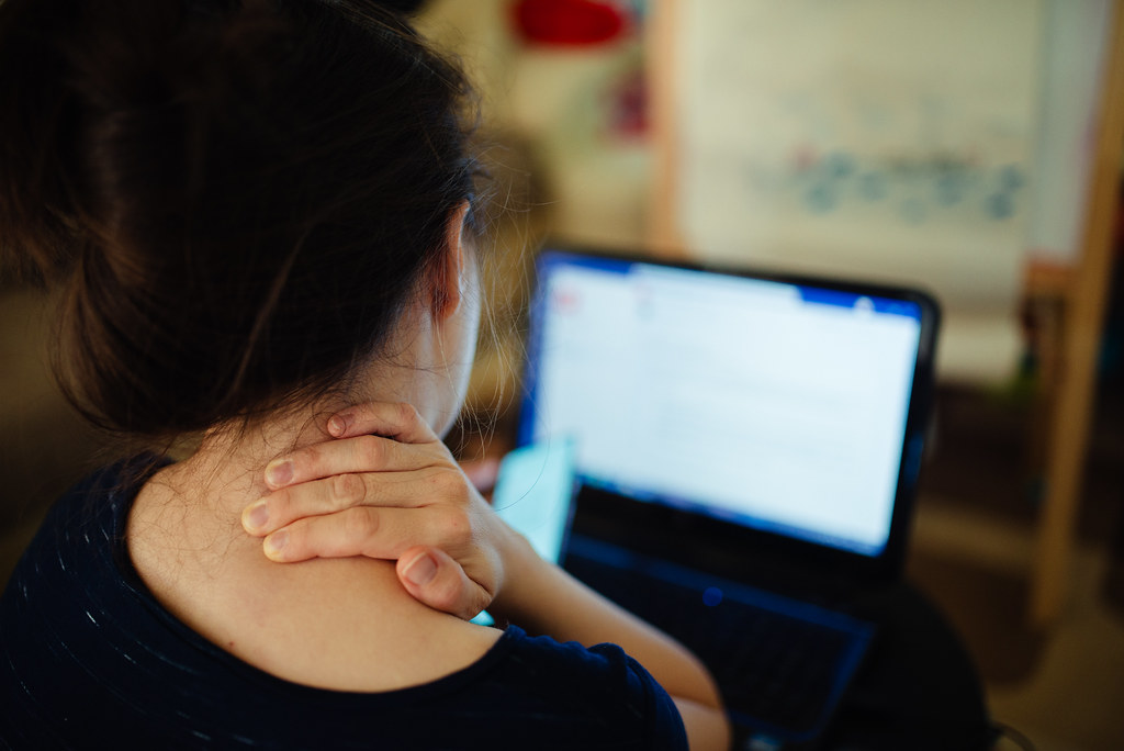 Woman experiencing neck pain while looking at her laptop.