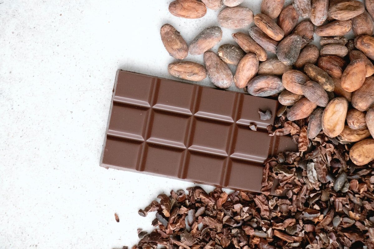 a bar of chocolate next to a pile of cocoa nibs & cocoa beans