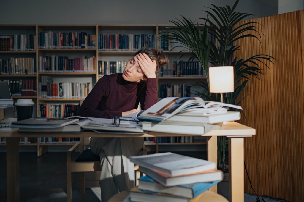 woman studying in library with dozens of books around her - She looks stressed