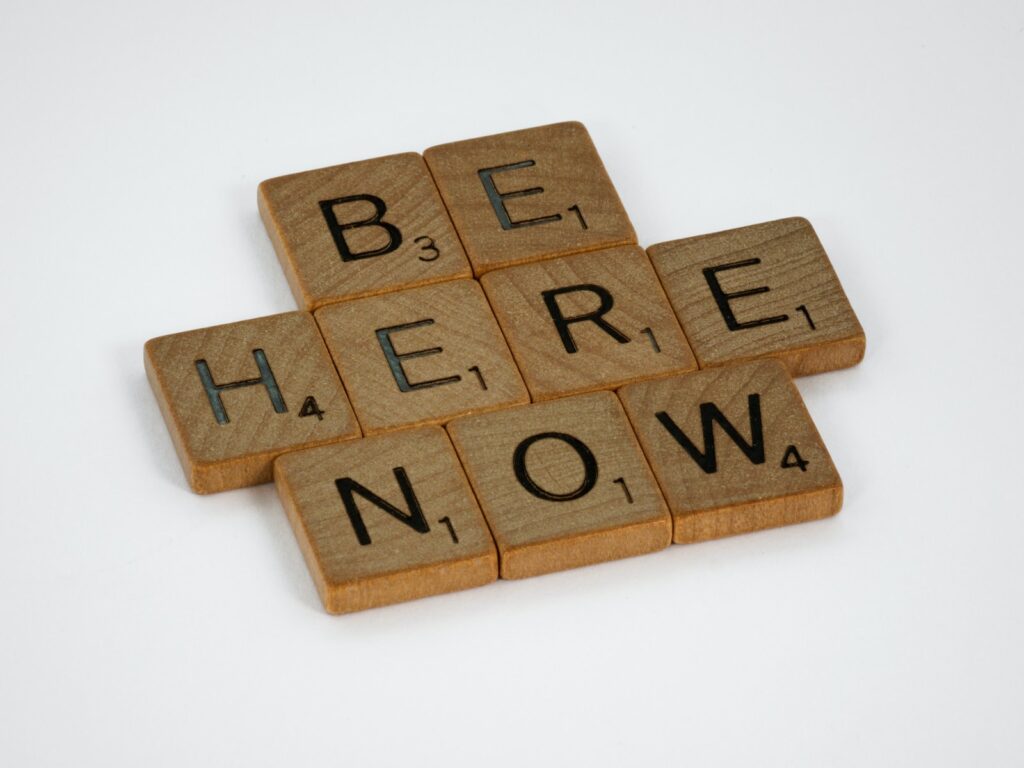 scrabble tiles that spell out "be here now"