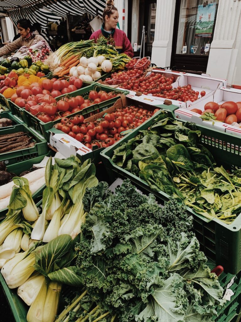 a variety of vegetables on display at a farmers market featuring kale and bok choy at the front. 