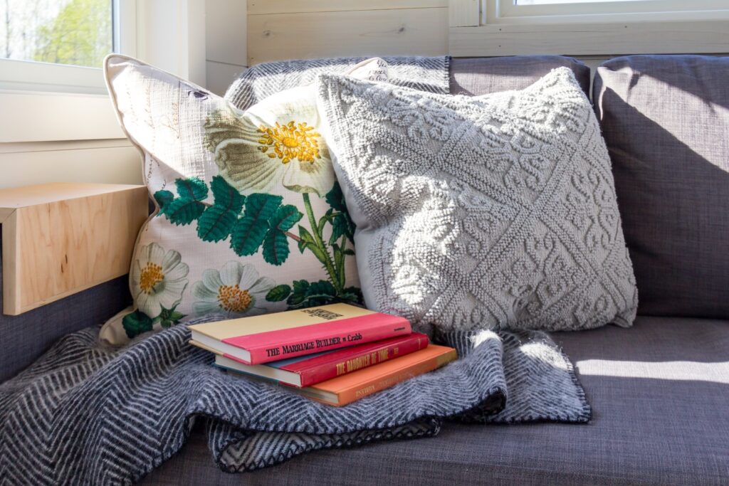 cozy spot on a grey couch with throw pillows, a blanket, and some books.