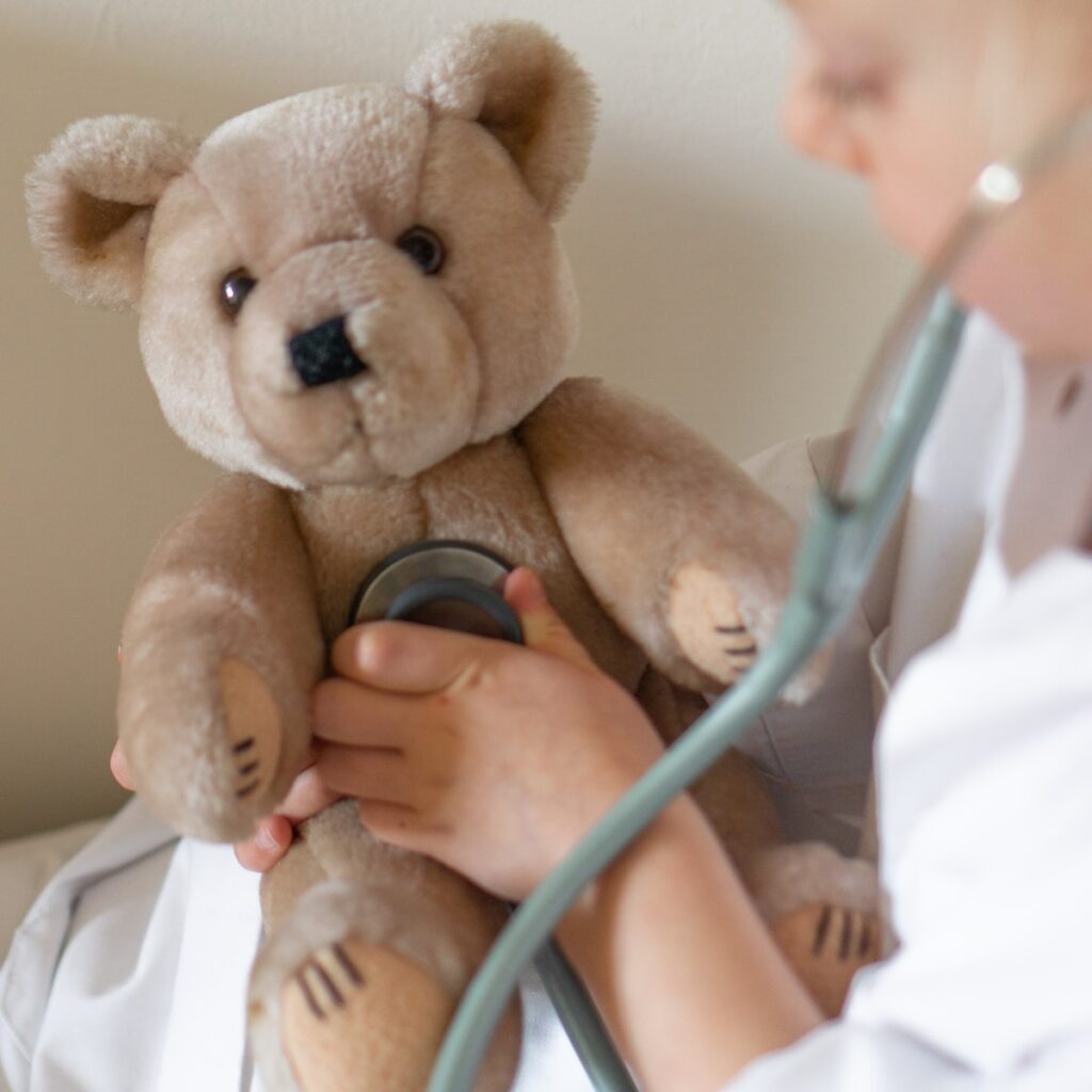 person holding stethoscope up to brown teddy bear