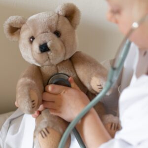 person holding stethoscope up to brown teddy bear