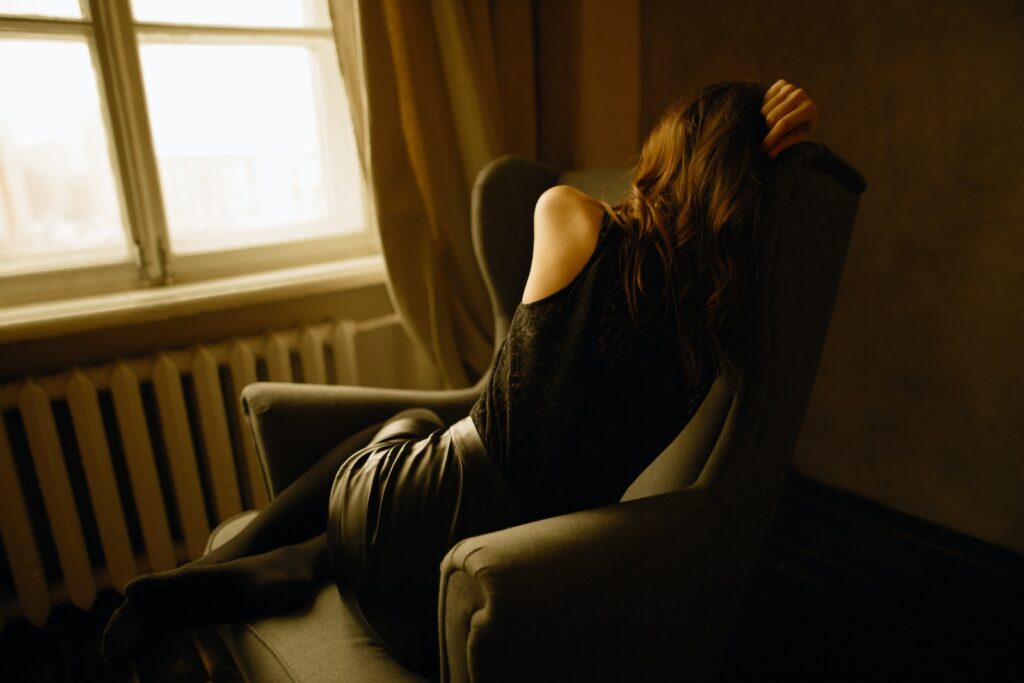 woman curled up in armchair sadly, looking out a window