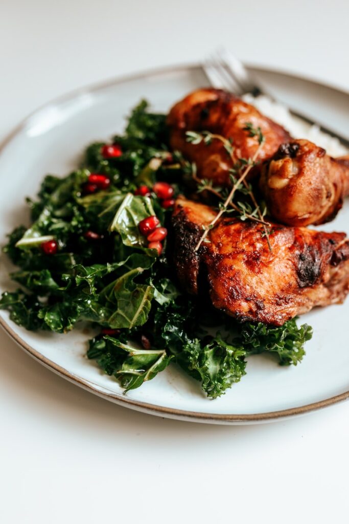 cooked chicken with kale and pomegranate seeds on white ceramic plate