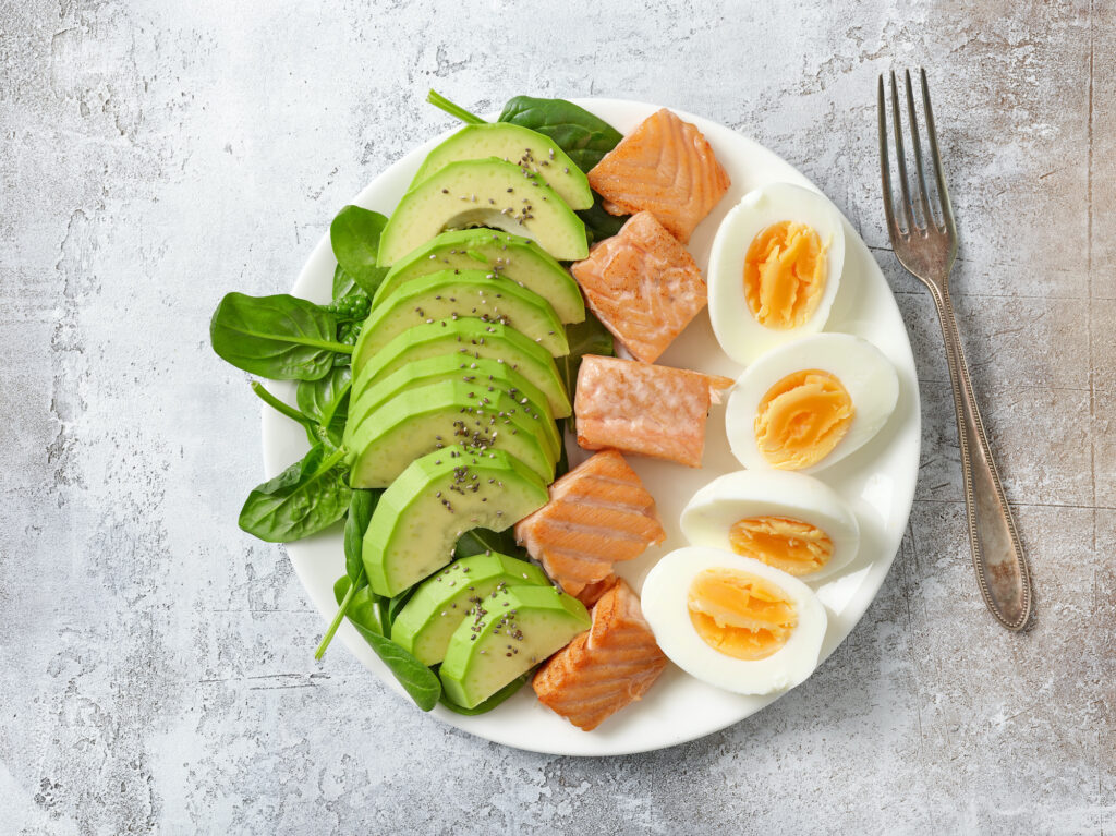 plate of Keto diet food ingredients on grey background, top view - sliced avocado, salmon, and eggs