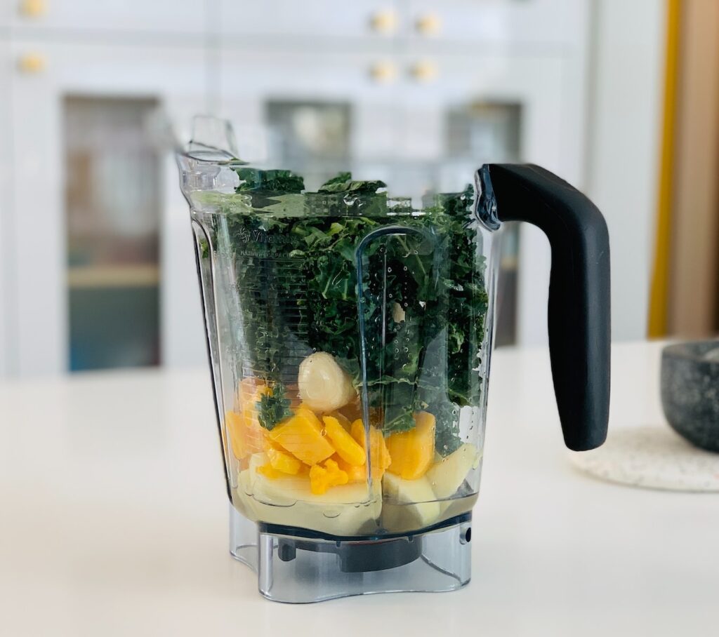 clear blender container full of kale, banana, and other fruits. 