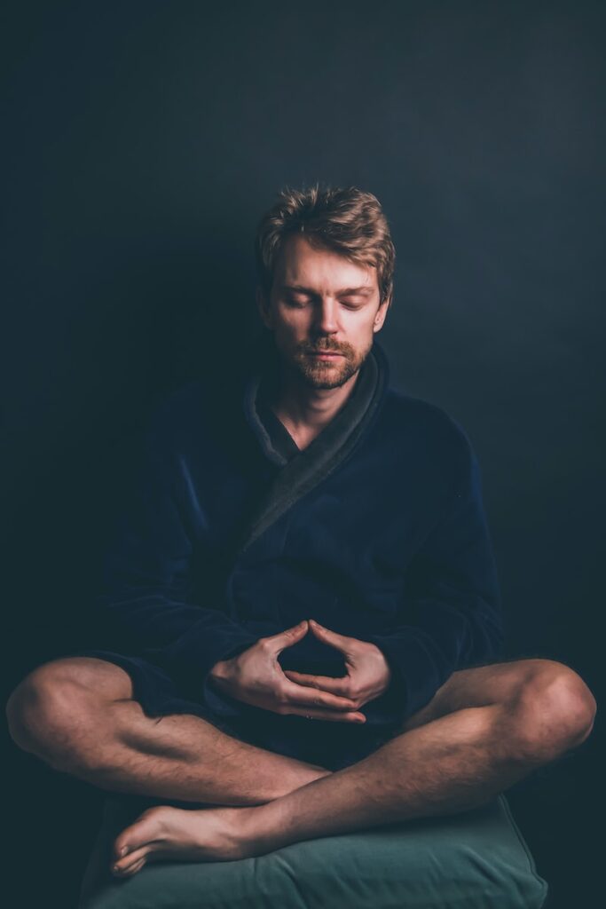 man in black hoodie sitting against black background meditating