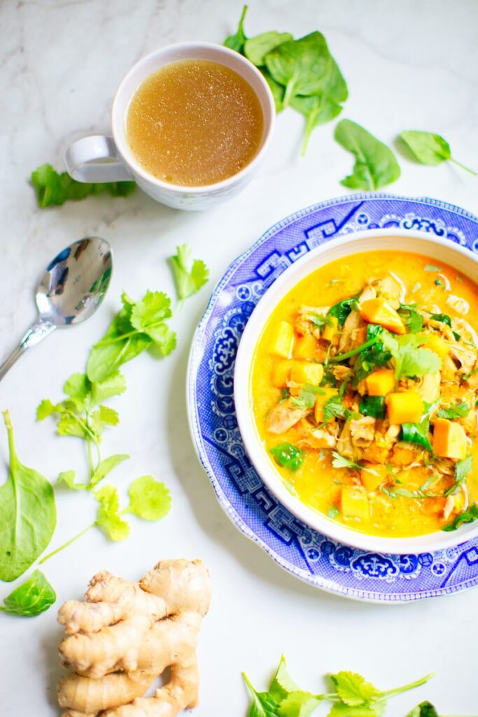 an orange vegetarian soup in a bowl with tea and a ginger root on the table