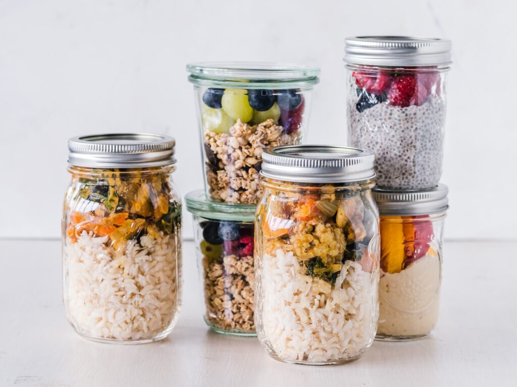 six glass jars full over fruits & overnight oats sitting on a white marble surface