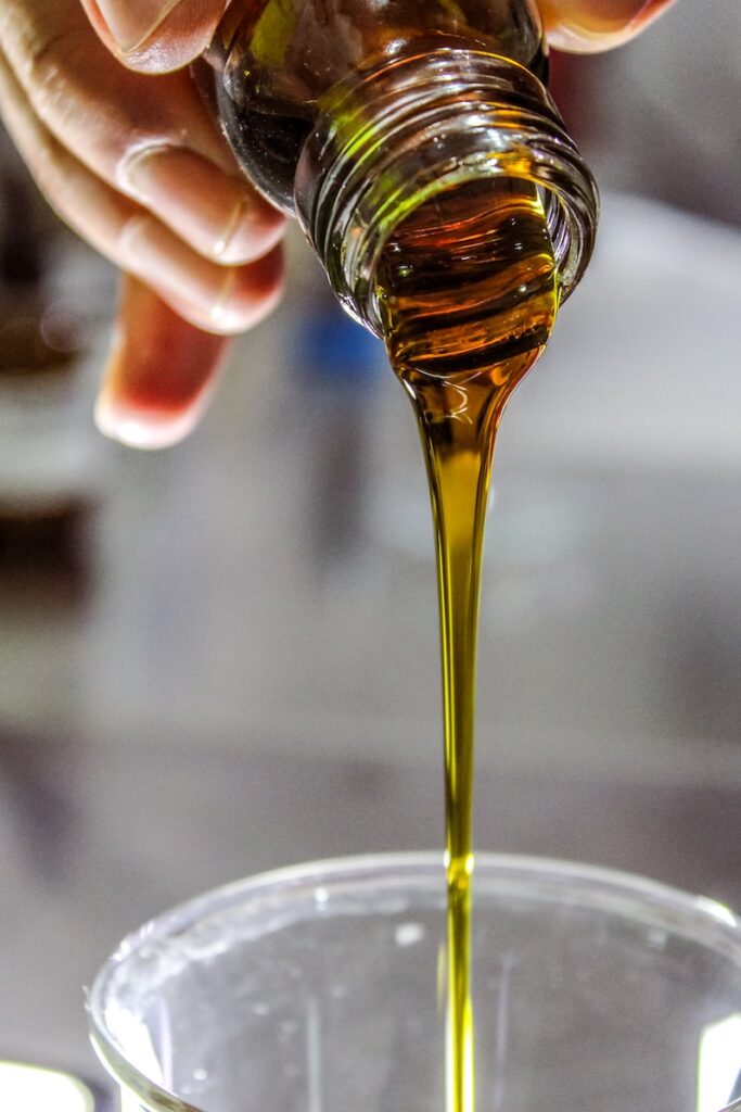 person pouring olive oil from small glass bottle into glass cup