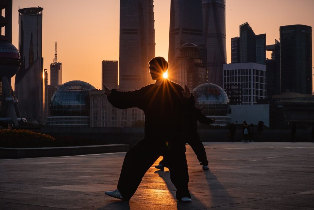 silhouette of person near buildings with sun shining through while practicing tai chi