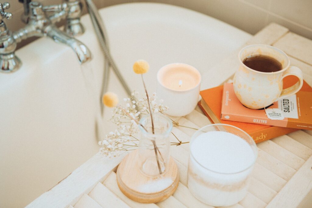 a bathtub with a bath tray holding some flowers, books, and tea.