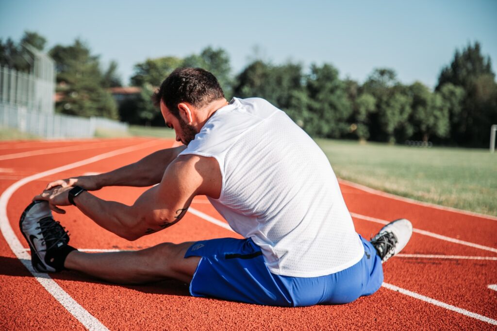 man in white sleeveless top stretching on a running track. He is flexible because he used hot therapy for his pain