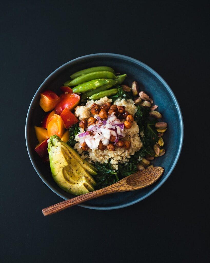 a blue bowl filled with cooked quinoa and vegetables and a wooden spoon