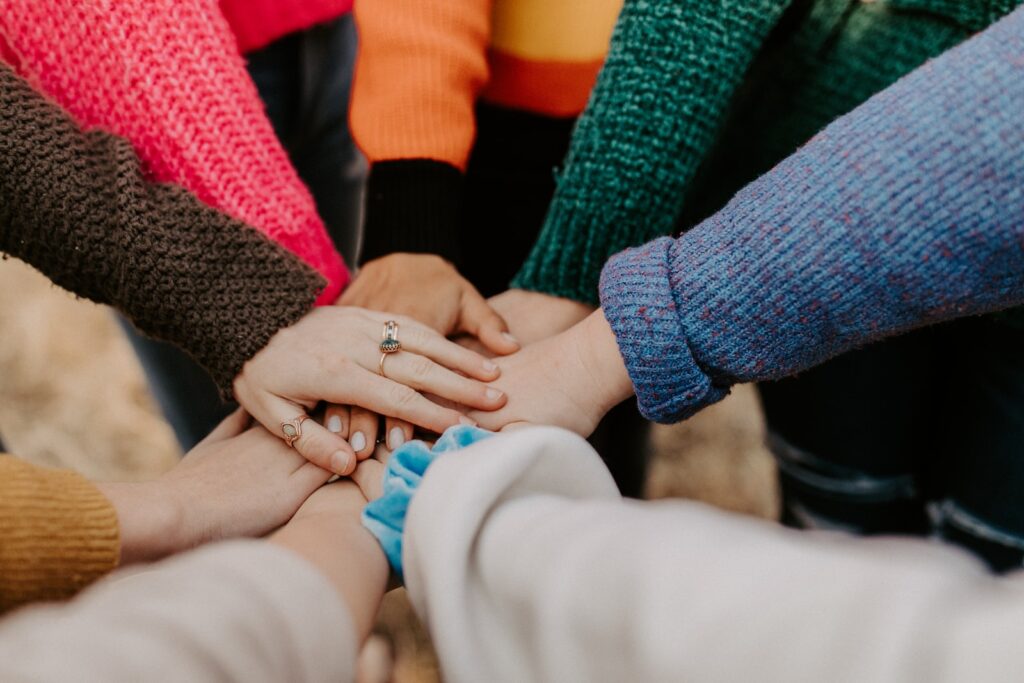 people standing in a circle placing their hands in the center supporting each other